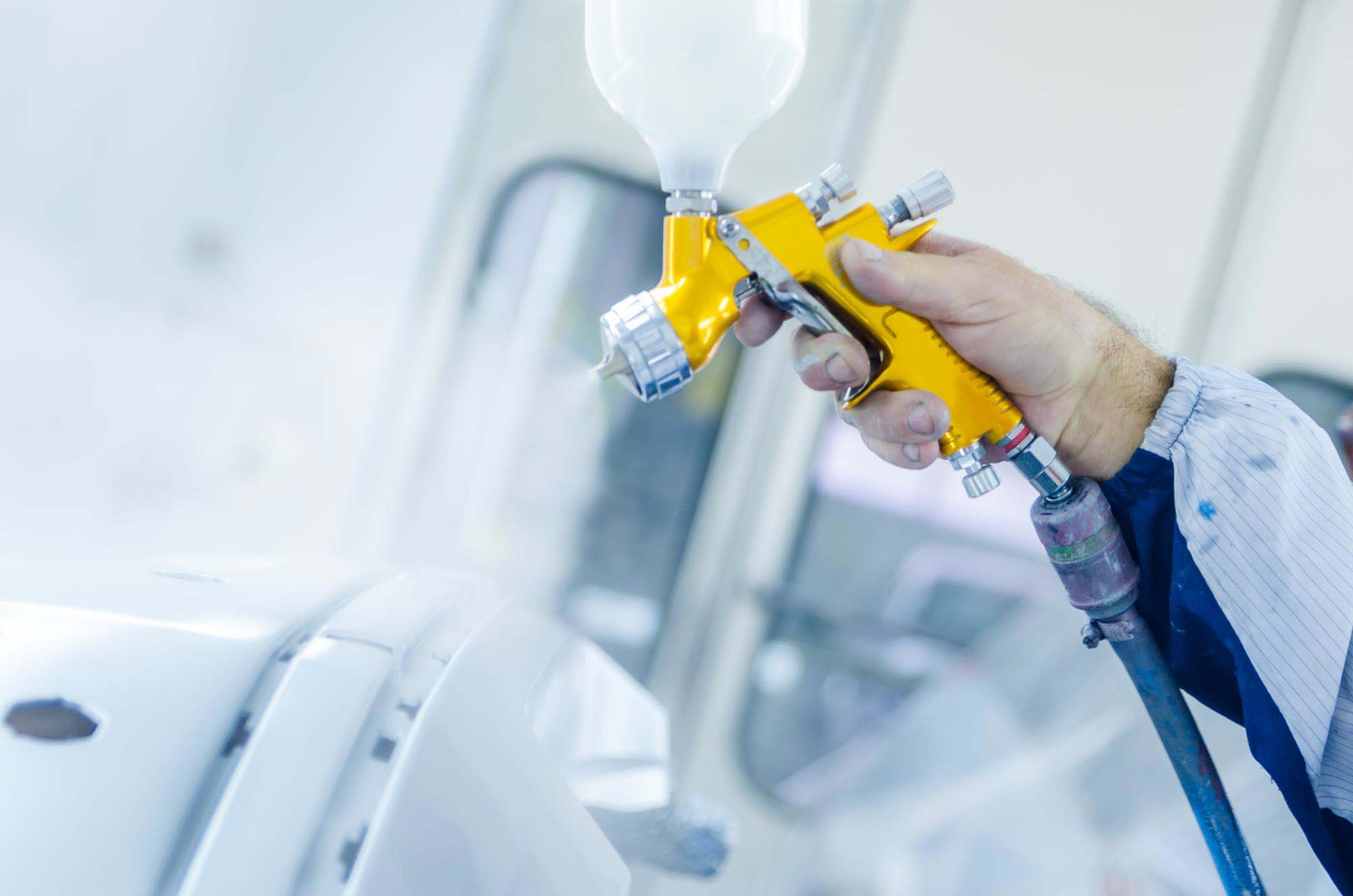 Painters gold paint gun spraying white bumper in booth – auto paint repair – hi tech auto collision & repair Painters gold paint gun spraying white bumper in booth - auto paint repair - hi tech auto collision & repair